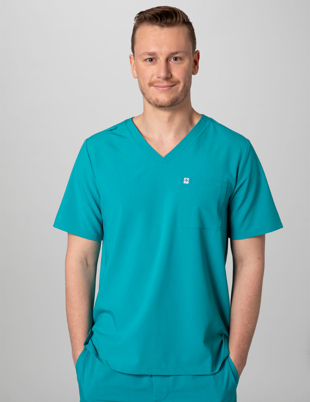 Care+Wear Men's 2-Pocket V-Neck Scrub Top in Teal, merging a refreshing color with essential storage for medical supplies. Model is wearing size Medium