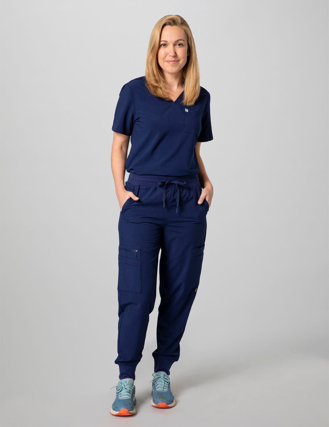 Care+Wear Women's 2-Pocket V-Neck Scrub Top in Navy, offering a professional style with practical storage for healthcare necessities. Model is wearing size Small