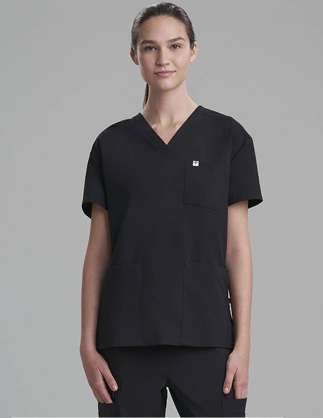 Care+Wear Women's 3-Pocket V-Neck Scrub Top in Black, combining sleek style with practical storage solutions for healthcare providers. Model is wearing size X-Small