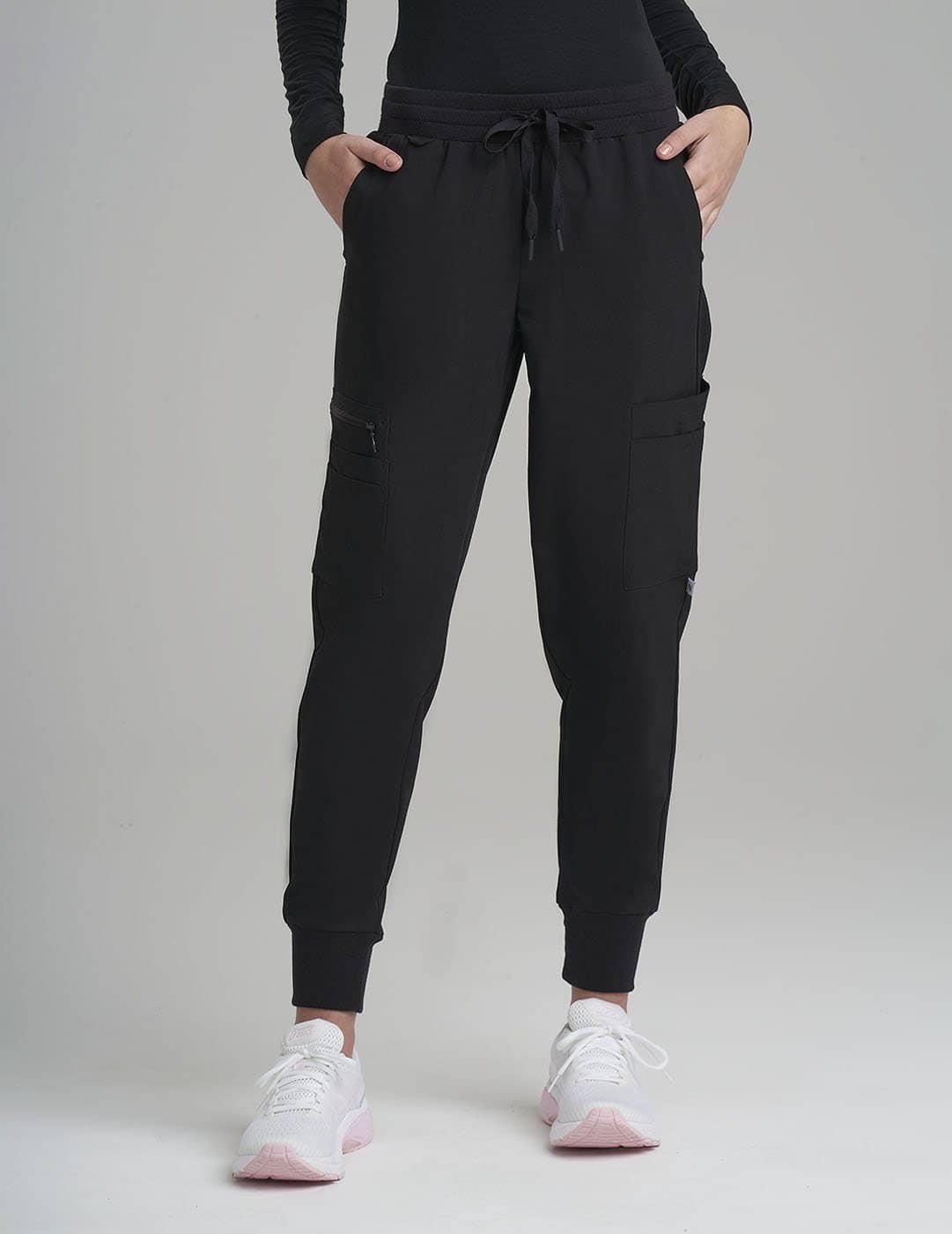 Classic Black Women's 12-Pocket Scrub Jogger Pants from Care+Wear, offering extensive storage and a sleek professional look. Model is wearing size X-Small
