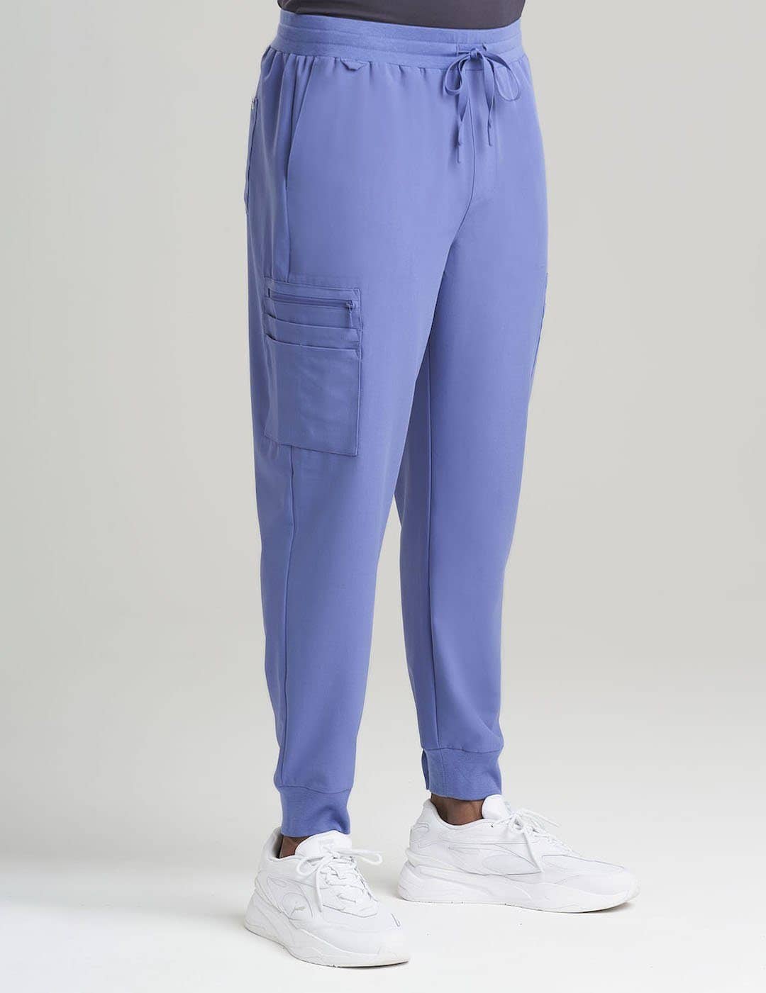 Ceil Men's 10-Pocket Jogger Scrub Pants by Care+Wear, featuring a light color and functional design for a relaxed yet professional look. Model is wearing size Large