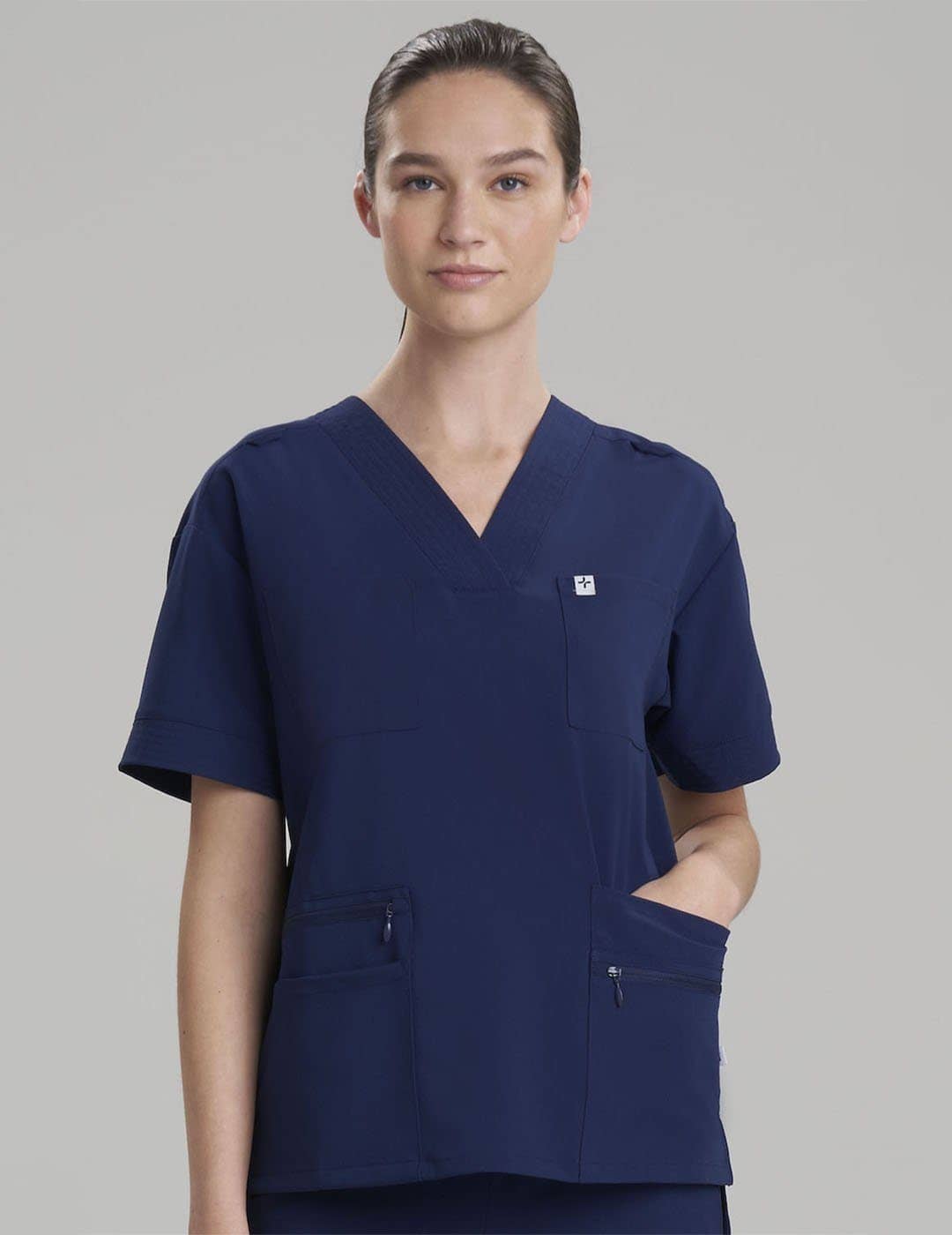 Royal blue women's scrub top with eight pockets, designed for functionality and professional wear. Model is wearing size X-Small