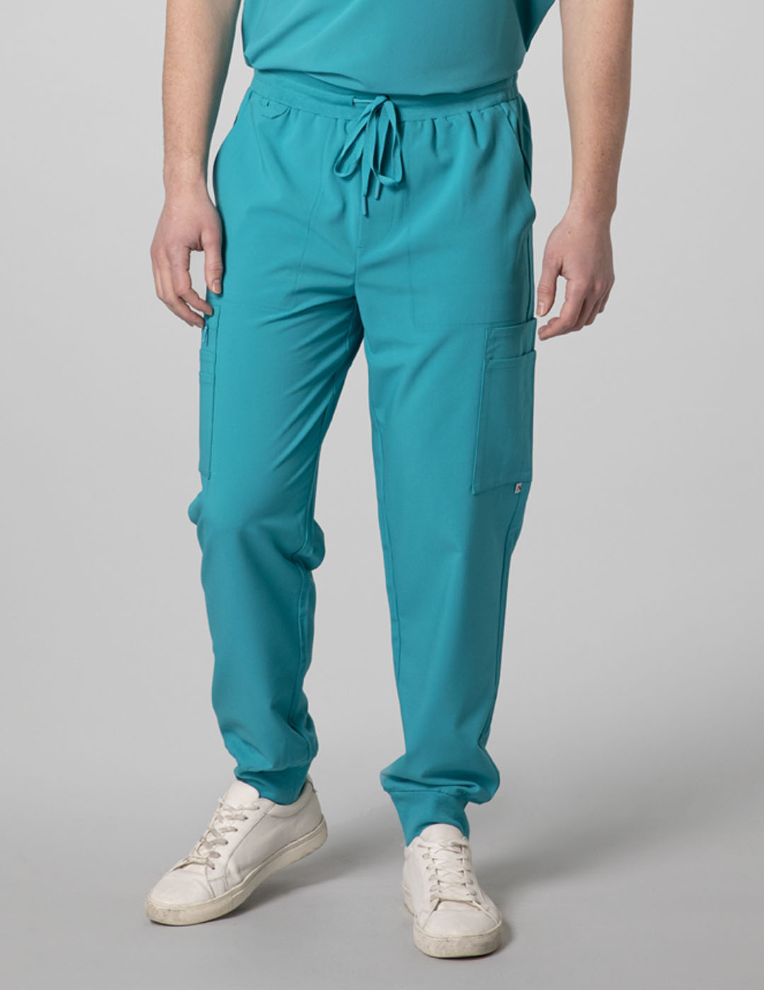 Care+Wear Men's 10-Pocket Jogger Scrub Pants in Teal, providing a relaxed fit with extensive storage options for healthcare workers. Model is wearing size Medium