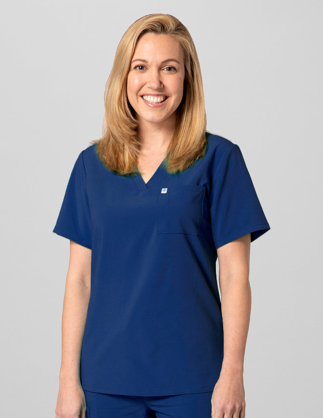 Care+Wear Women's 2-Pocket V-Neck Scrub Top in Navy, offering a professional style with practical storage for healthcare necessities. Model is wearing size Small