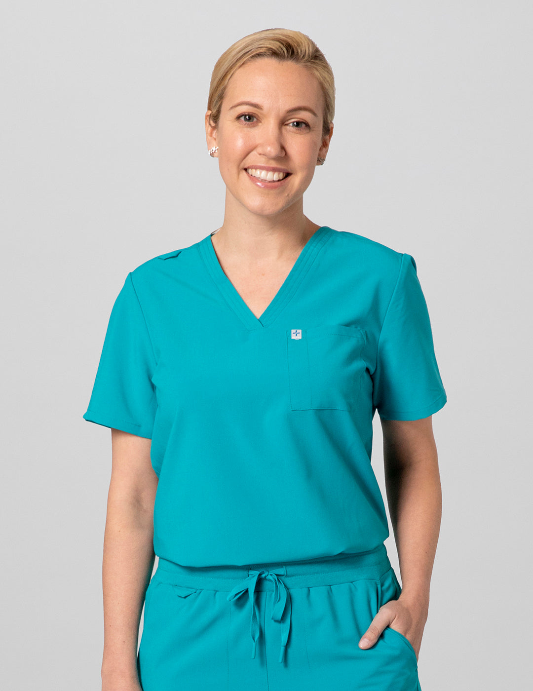 Care+Wear Women's 2-Pocket V-Neck Scrub Top in Teal, combining a calming hue with functional design for medical professionals. Model is wearing size Small