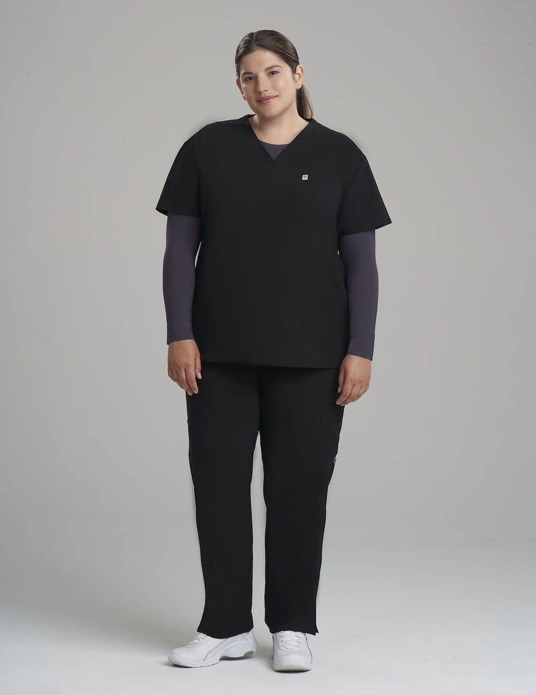 Comfortable and durable stone gray scrub top for women, featuring a V-neck and three ample storage pockets. Model is wearing size Large
