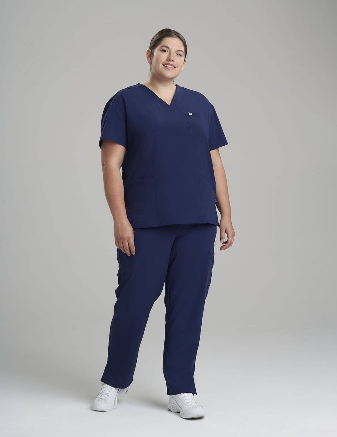 Versatile women&#39;s scrub top in stone gray, offering a clean V-neck design and three pockets for storage. Model is wearing size Large