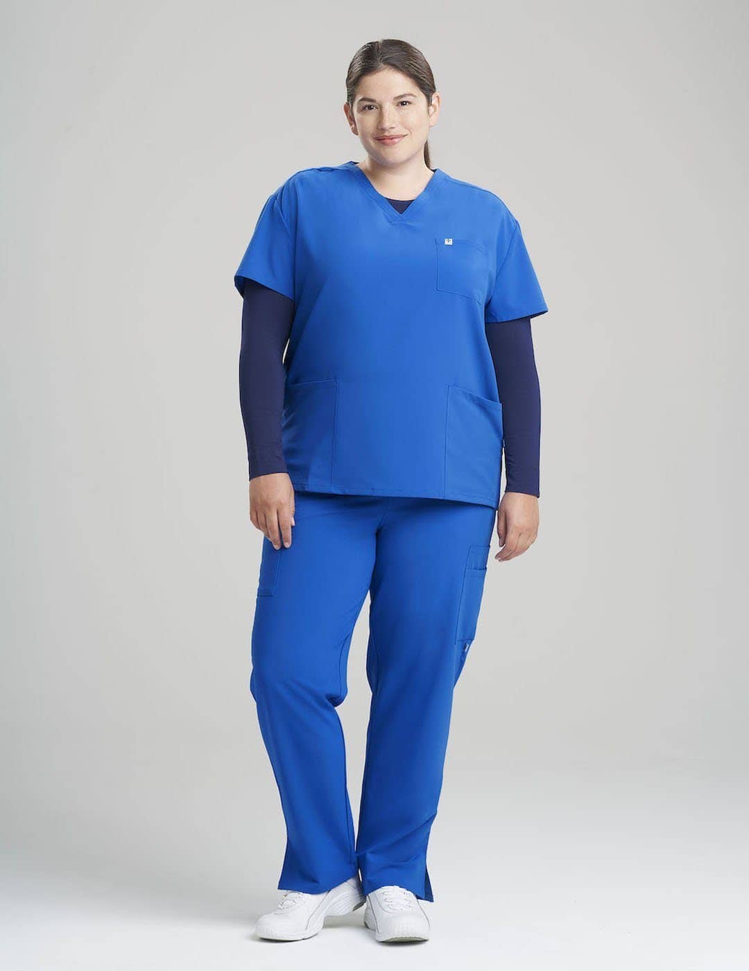 Limited Edition Ceil Women&#39;s 3-Pocket V-Neck Scrub Top by Care+Wear, featuring unique color and ample pockets for functional medical wear. Model is wearing size Large