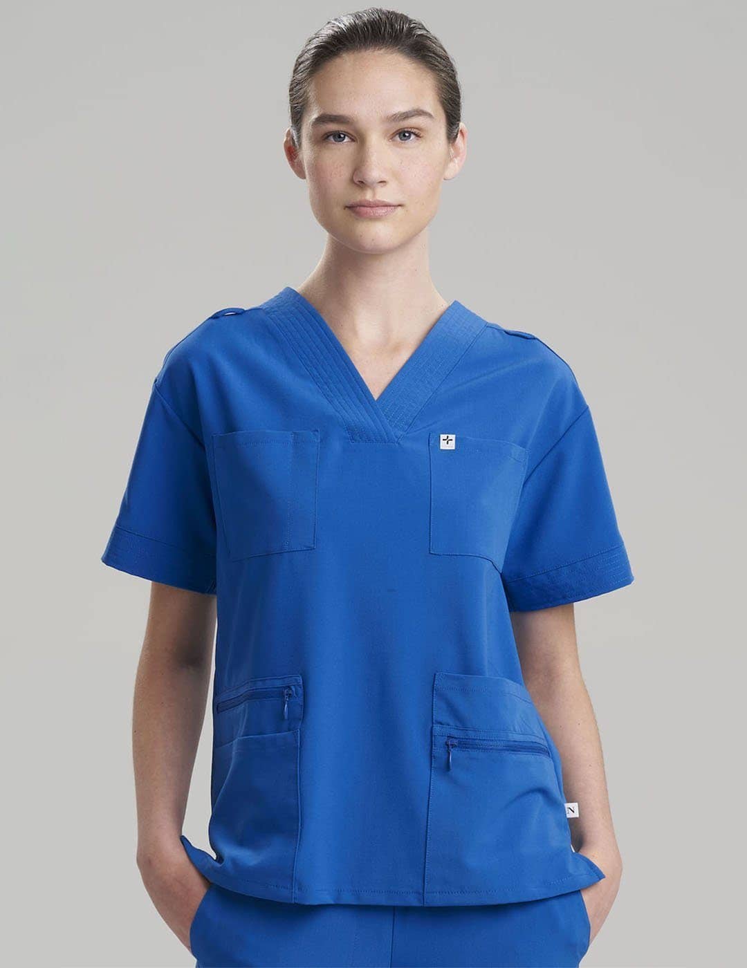Functional women's V-neck scrub top in royal blue, designed with eight pockets for organized storage. Model is wearing size X-Small